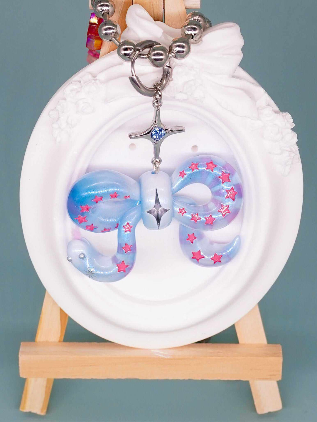Ice blue snake bowtie necklace with pink star accents and silver chain on a white decorative frame
