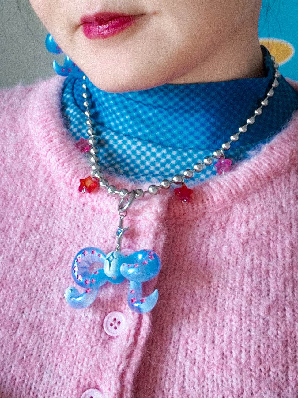 Close-up of person wearing ice blue snake bowtie necklace with pink star accents and silver beads