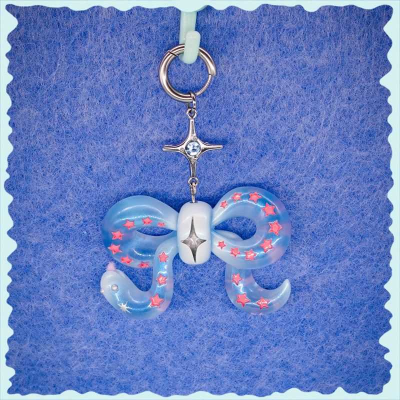Ice blue snake bowtie necklace with pink star accents and silver star charm on blue background
